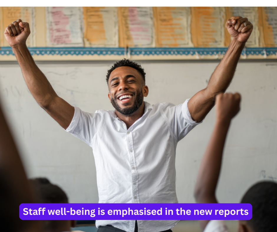 A male teacher standing smiling with his hands in the arm in triumph in front of a class of children
